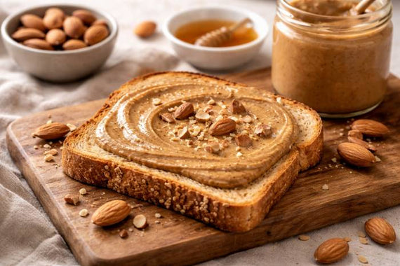 Almond butter spread over whole grain toast with almonds and honey nearby
